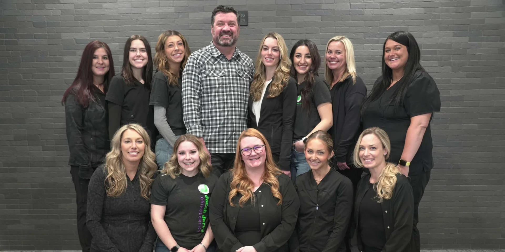 Smiling orthodontic team in black uniforms posed with bearded male doctor in plaid shirt